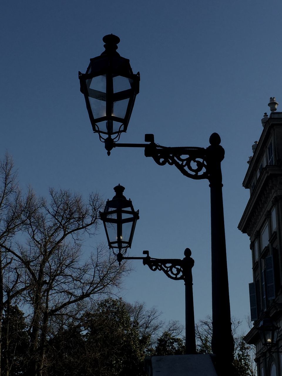 low angle view, silhouette, statue, clear sky, sculpture, human representation, street light, art and craft, art, lighting equipment, creativity, built structure, sky, dusk, architecture, outdoors, building exterior, lamp post