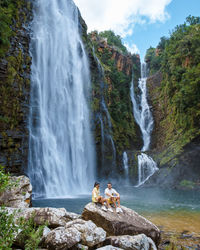 Rear view of man sitting against waterfall