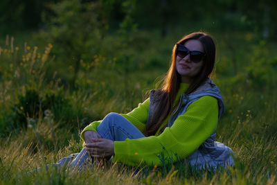 Portrait of young woman wearing sunglasses sitting on field