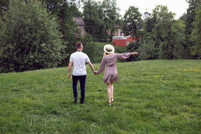 Man and a woman in love in a dress and hat are walk on a green field under a tree in summer