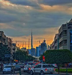 Cars moving on road against buildings at sunset