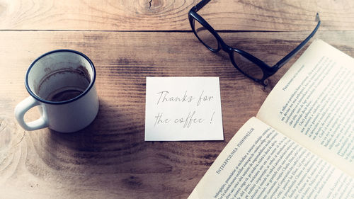 High angle view of coffee cup on table with book and eyeglasses and text message on place of paper