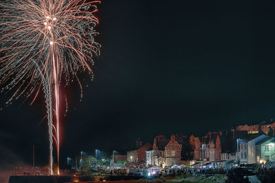 Firework display in city against sky at night