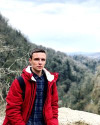 Portrait of young man standing on mountain against cloudy sky