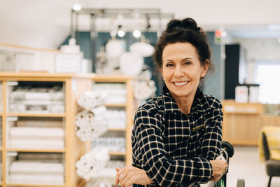 Portrait of smiling senior woman with arms crossed standing in store