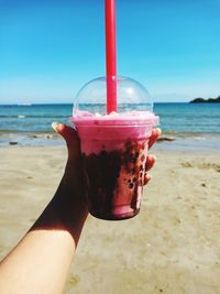 Cropped hand holding drink at beach