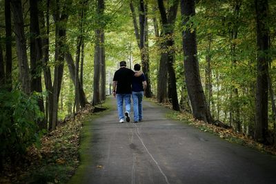 Rear view of grandfather and son walking on road amidst trees at forest