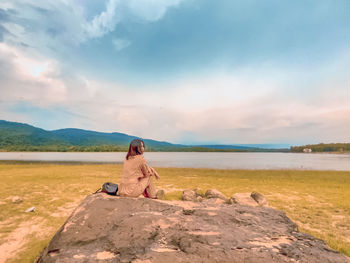 Woman sitting on land against sky