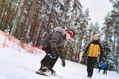 Full length of boy snowboarding on snow against trees