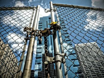 Low angle view of buildings seen through locked chainlink fence