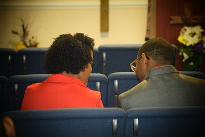 Rear view of man and woman sitting on chairs in church
