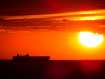 Silhouette boat in sea against orange sky