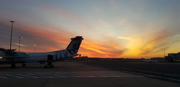 Airplane on airport runway against sky during sunset