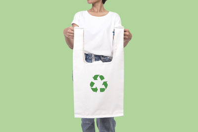 Midsection of woman holding shopping bag with recycling symbol while standing against green background