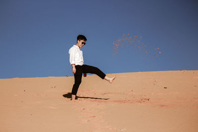 Full length of woman kicking sand at desert against clear sky
