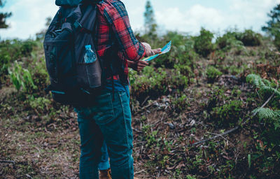 Midsection of man with friend discussing map while standing by plants against sky