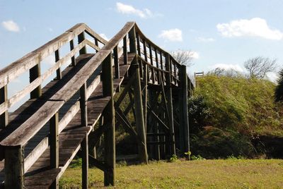 Wooden footbridge over field against sky