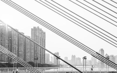 Low angle view of modern buildings seen through cables against clear sky