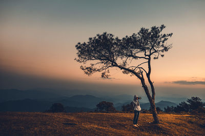 Young man photographing while standing on mountain against sky during sunset