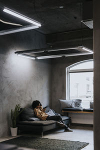 Female entrepreneur using mobile phone while sitting on sofa at creative workplace