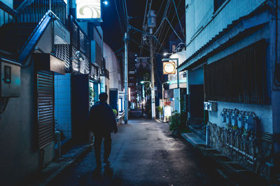 Rear view of man walking on street amidst buildings in city at night