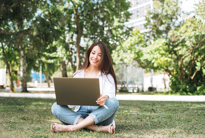 Woman using laptop while sitting on field