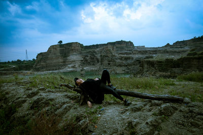 Woman relaxing on wood over land against sky