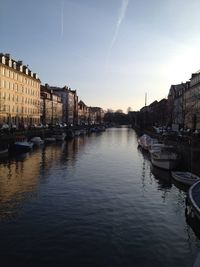 Boats moored in canal by buildings against sky in city