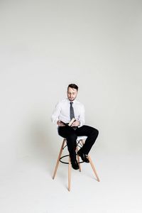Man reading book while sitting on chair against white background