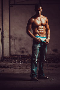 Portrait of shirtless male athlete standing against wall