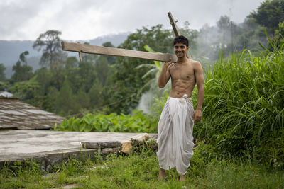 Happy indian farmer standing with wooden plough in rice field