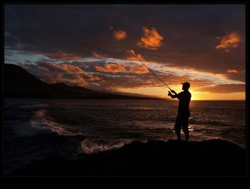 Silhouette of people standing on beach at sunset