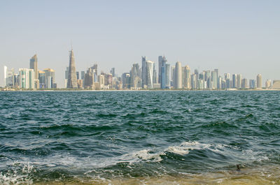 Sea by modern buildings against clear sky