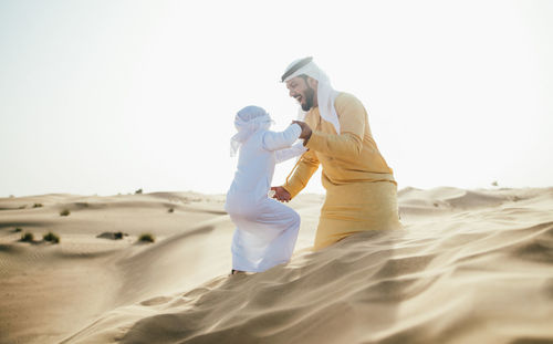 Friends standing on sand dune in desert against sky