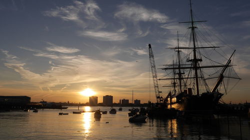 Hms warrior a vintage battleship is seen at sunset. many boats and buildings can be seen too.