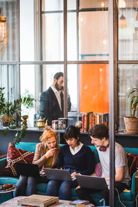 Confident colleagues discussing over laptop against businessman in creative office