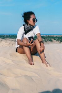 Young woman wearing sunglasses on beach against clear sky