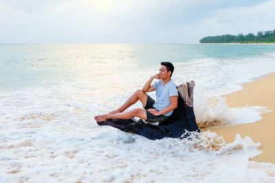 Full length of young woman relaxing on beach against sky