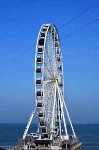 Ferris wheel in sea against clear blue sky