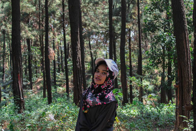 Portrait of woman standing against trees in forest