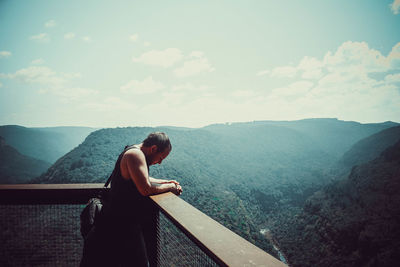 Side view of woman standing on mountain against sky