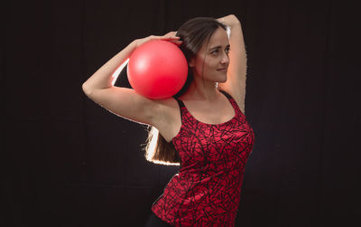 Mid adult woman holding fitness ball against black background