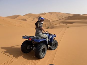 Rear view of man sitting on sand at desert