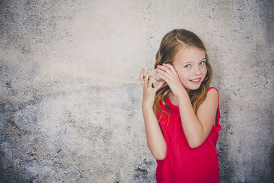 Cute smiling girl playing with tin can phone while standing against wall