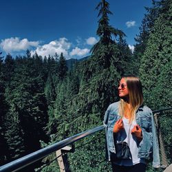Young woman standing by railing against sky