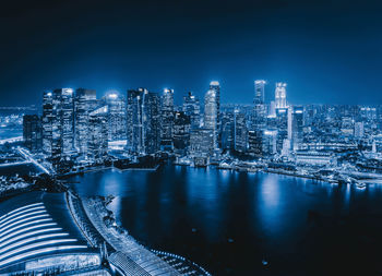 River by illuminated cityscape against sky at night