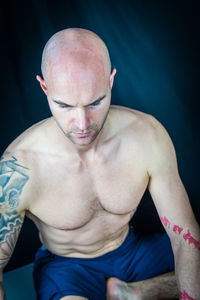 Shirtless bald man doing yoga against black background