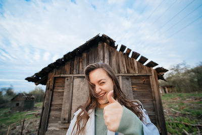 Beautiful girl with long hair in a grey trench coat next to an old wooden house outdoors in spring