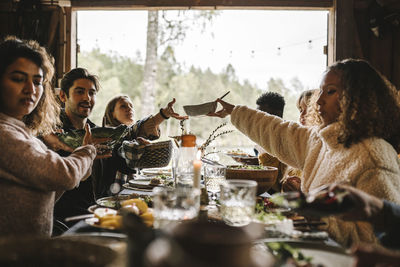 Female passing food bowl to friend over table during social event