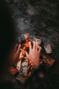 High angle view of cropped hands over bonfire